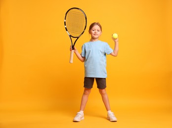 Photo of Cute little girl with tennis racket and ball on pink background