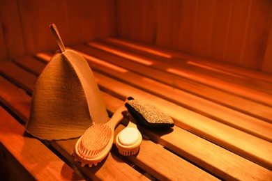 Felt wool hat and bath accessories on wooden bench in sauna. Space for text