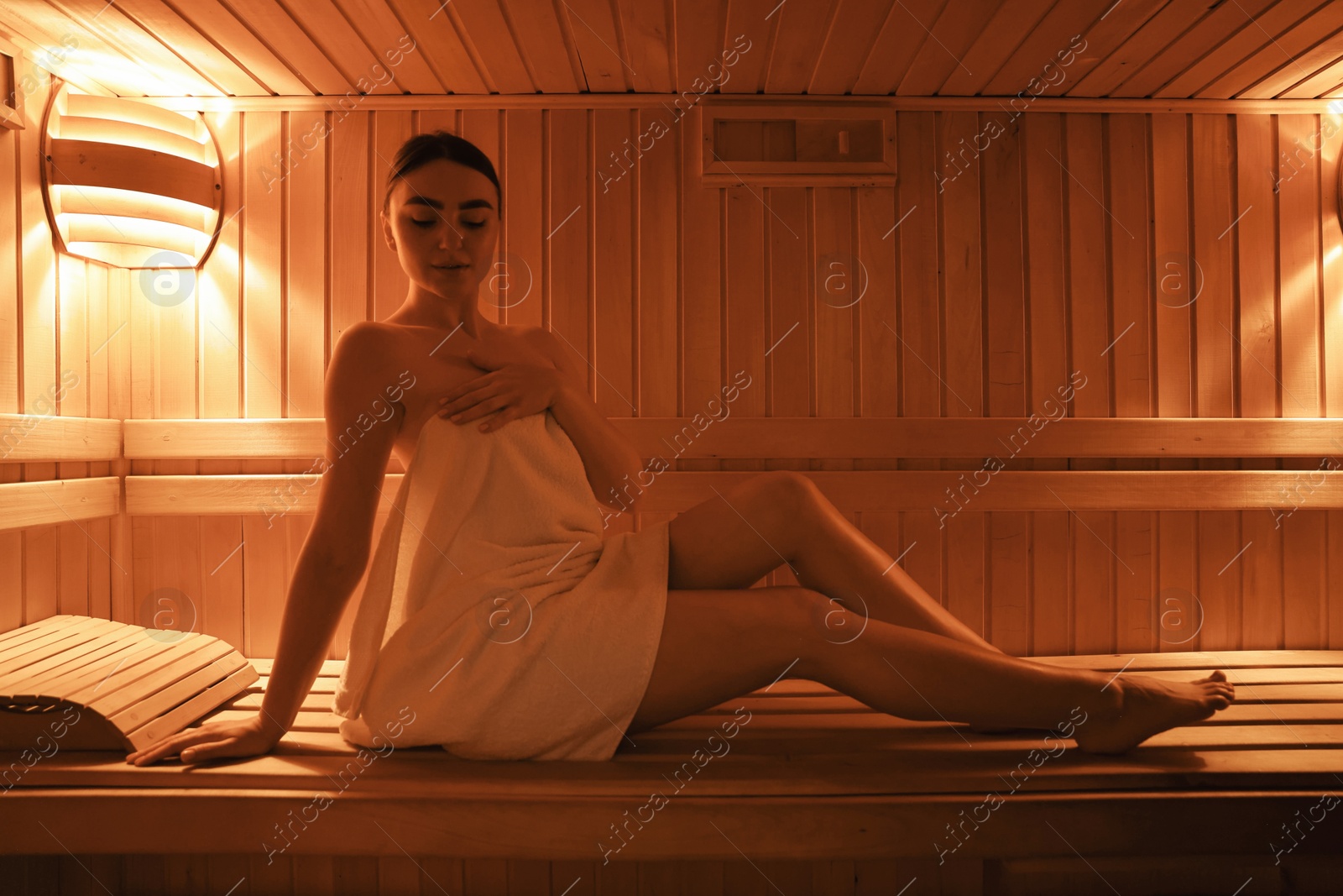 Photo of Beautiful woman wrapped in towel on bench at sauna