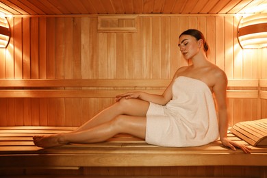 Photo of Beautiful woman wrapped in towel on bench at sauna