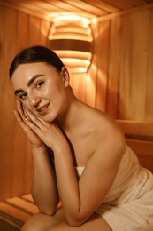 Beautiful woman wrapped in towel on bench at sauna