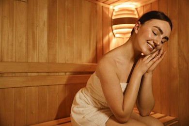 Beautiful woman wrapped in towel on bench at sauna. Space for text