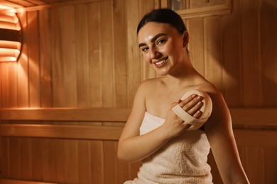 Photo of Smiling woman with massage sponge in sauna. Space for text