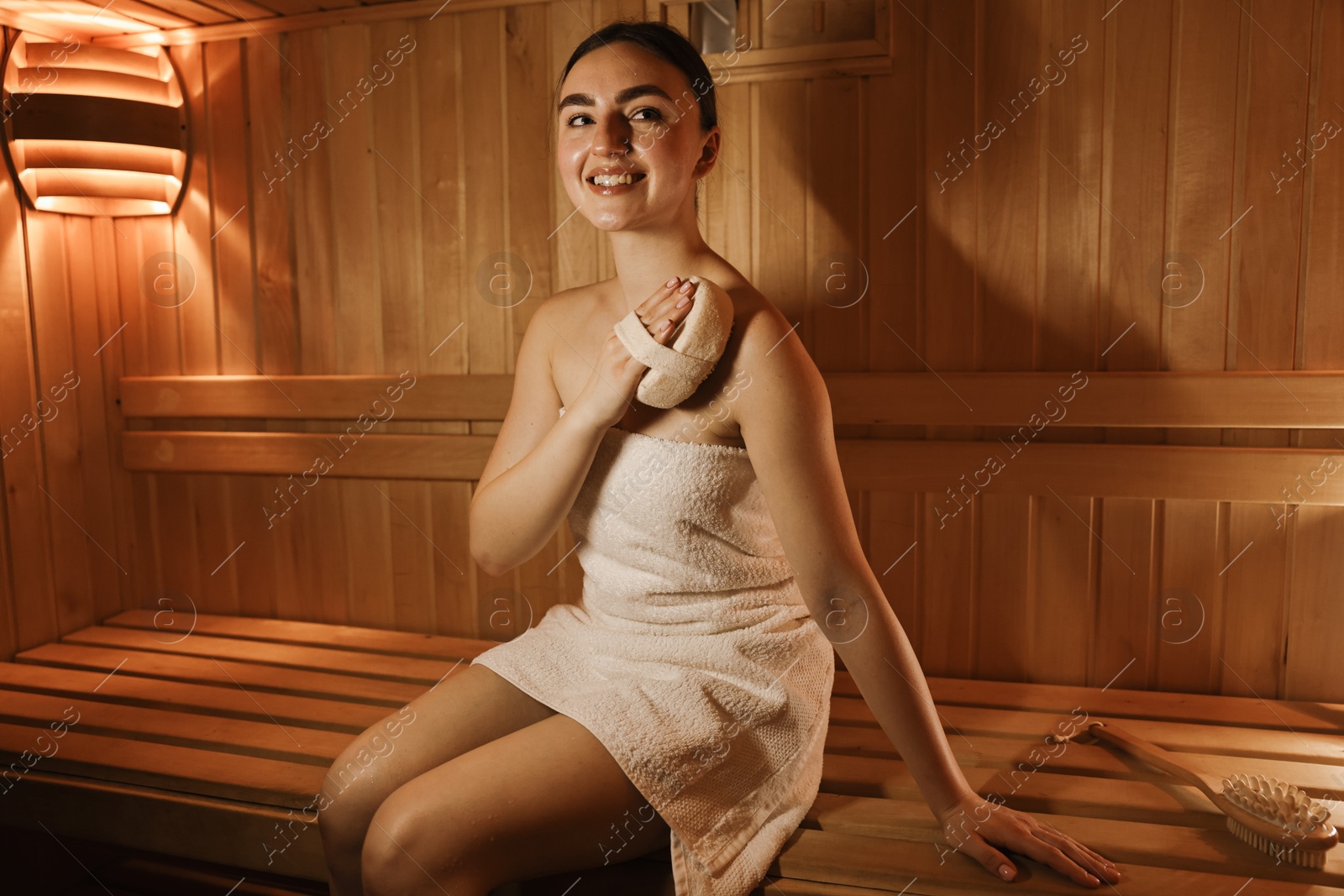 Photo of Woman with massage sponge on bench in sauna