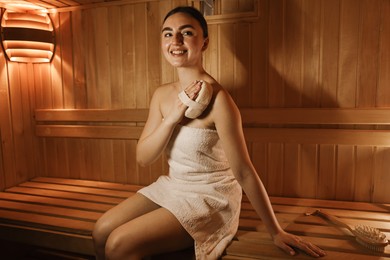 Photo of Woman with massage sponge on bench in sauna