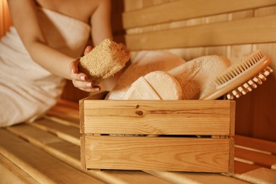 Woman with bath accessories on wooden bench in sauna, closeup