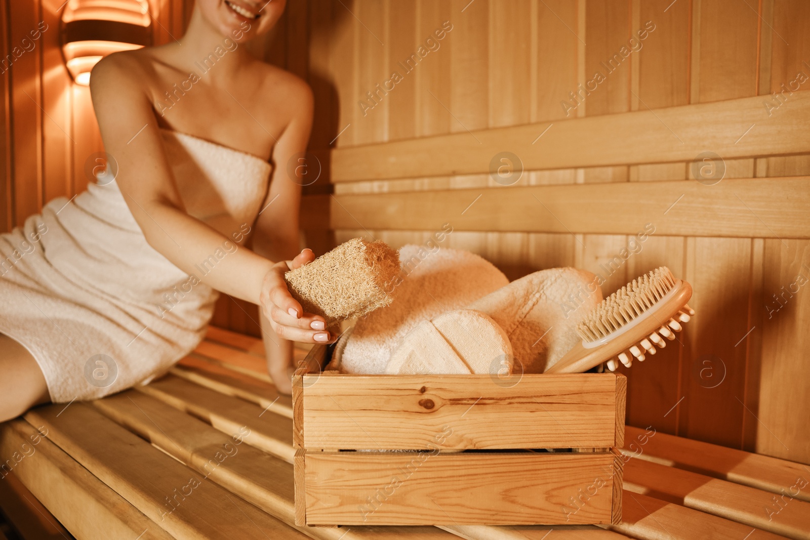 Photo of Woman with bath accessories on wooden bench in sauna, closeup