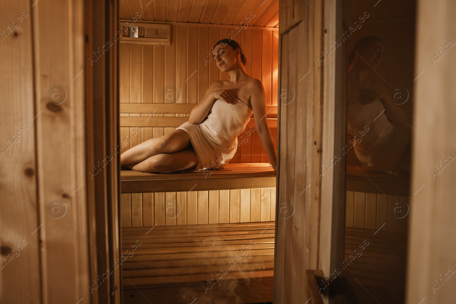 Photo of Beautiful woman wrapped in towel on bench at sauna