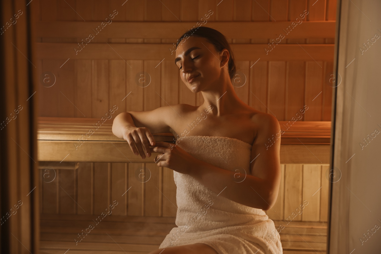 Photo of Beautiful woman wrapped in towel on bench at sauna