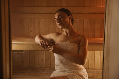 Photo of Beautiful woman wrapped in towel on bench at sauna