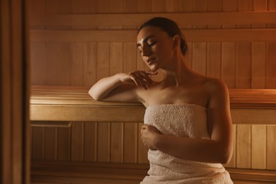 Photo of Beautiful woman wrapped in towel on bench at sauna