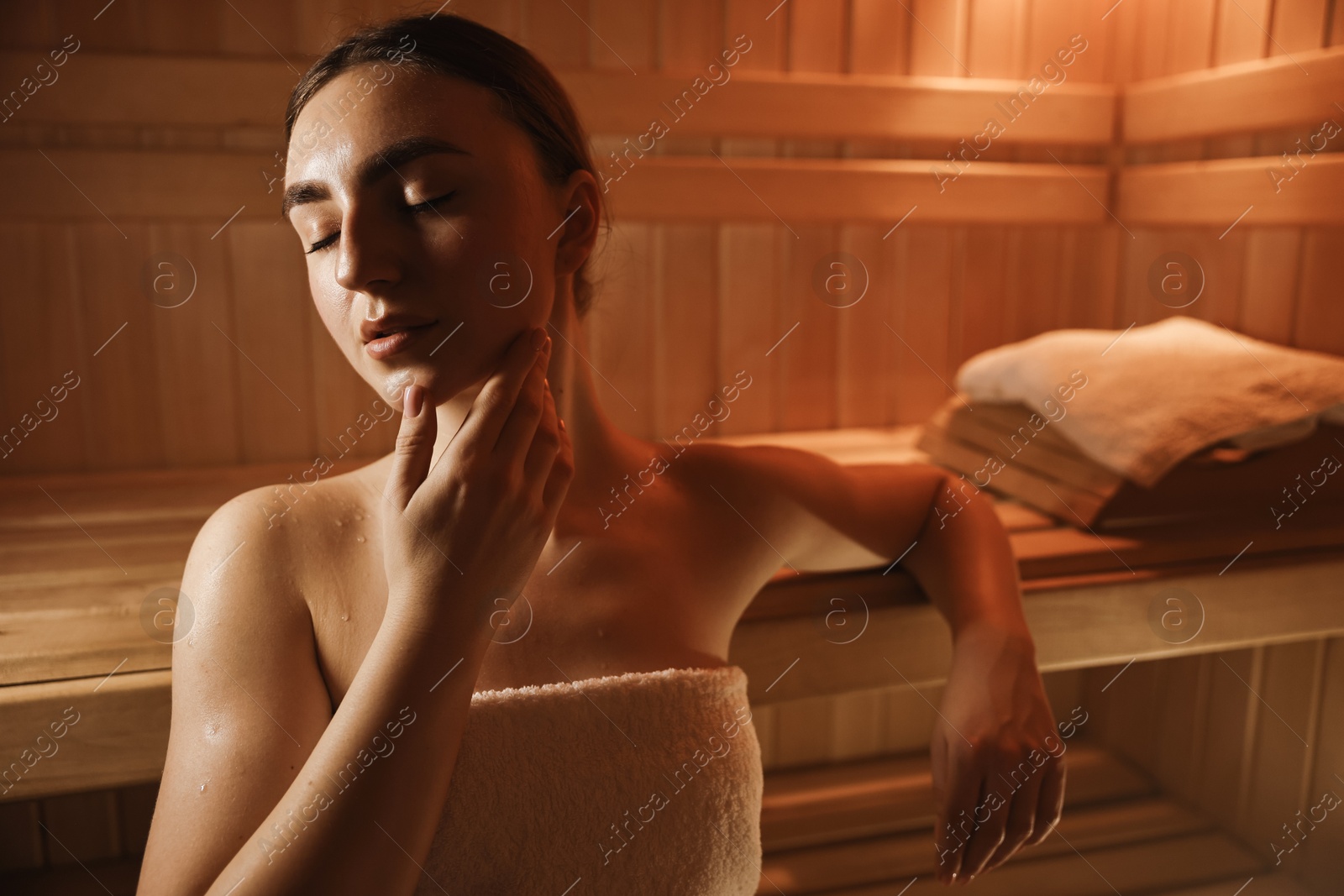 Photo of Beautiful woman wrapped in towel on bench at sauna