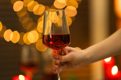 Photo of Woman with glass of red wine against blurred lights, closeup. Romantic dinner