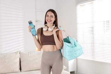 Happy woman with gym bag and water bottle at home