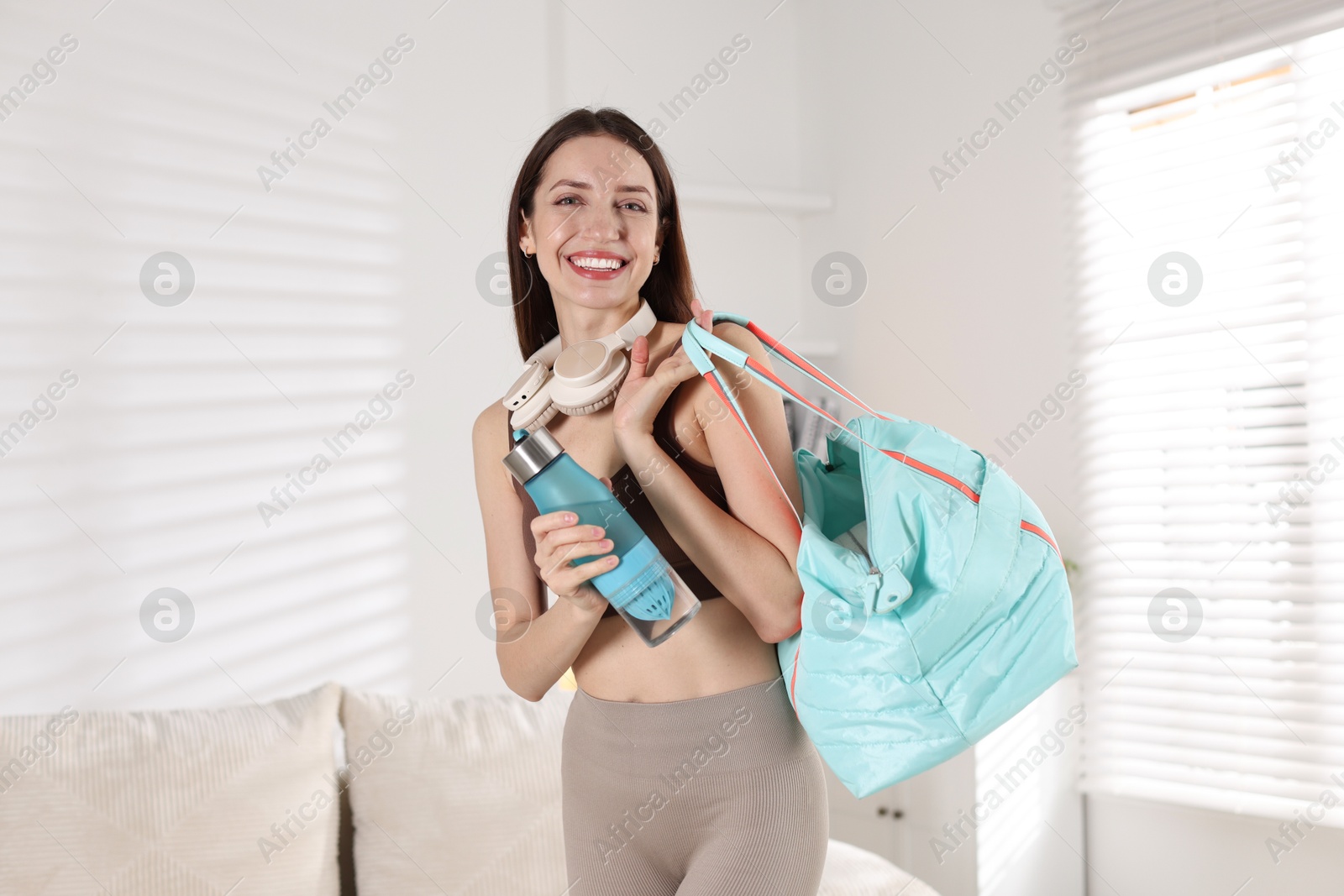 Photo of Happy woman with gym bag and water bottle at home