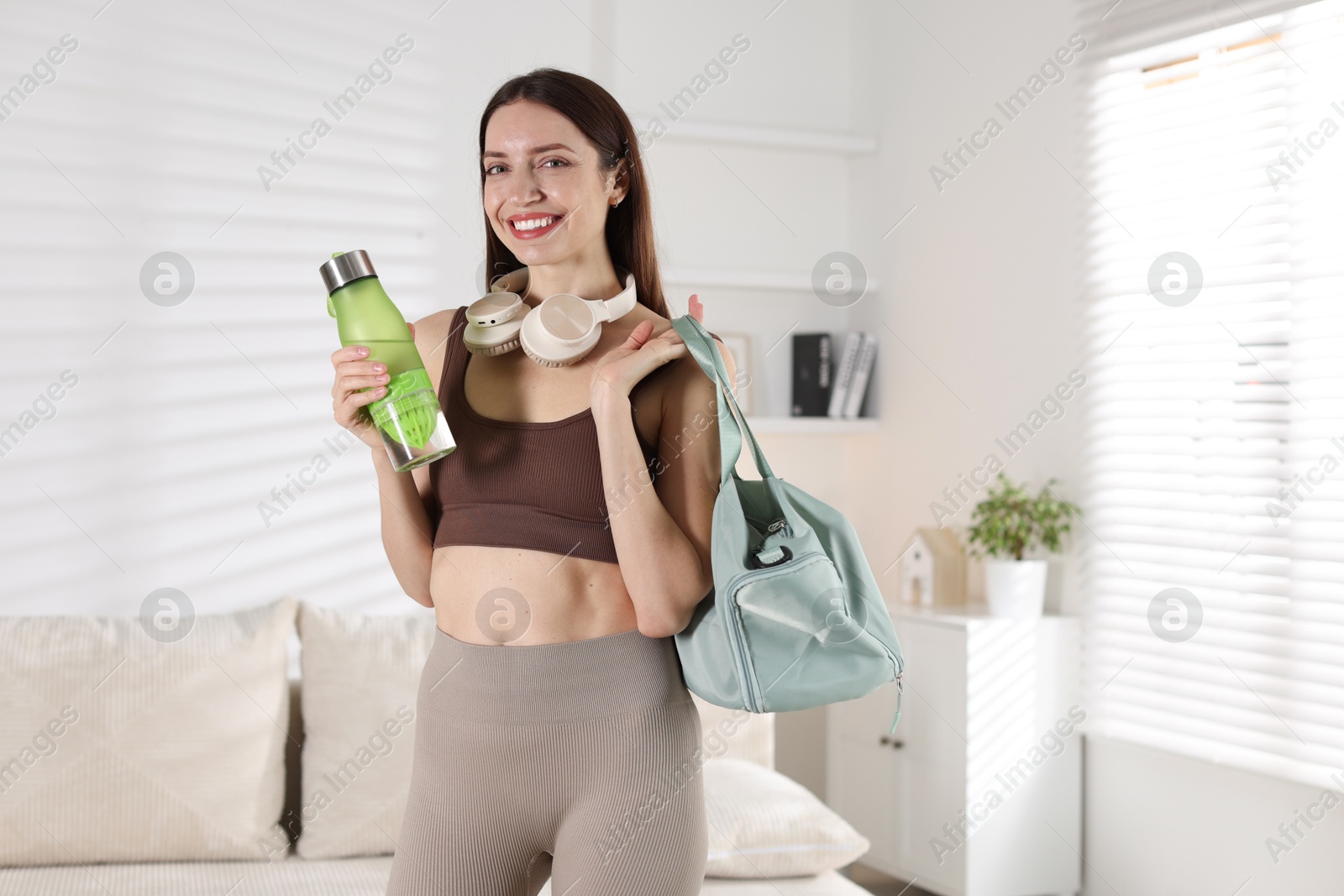 Photo of Happy woman with gym bag and water bottle at home