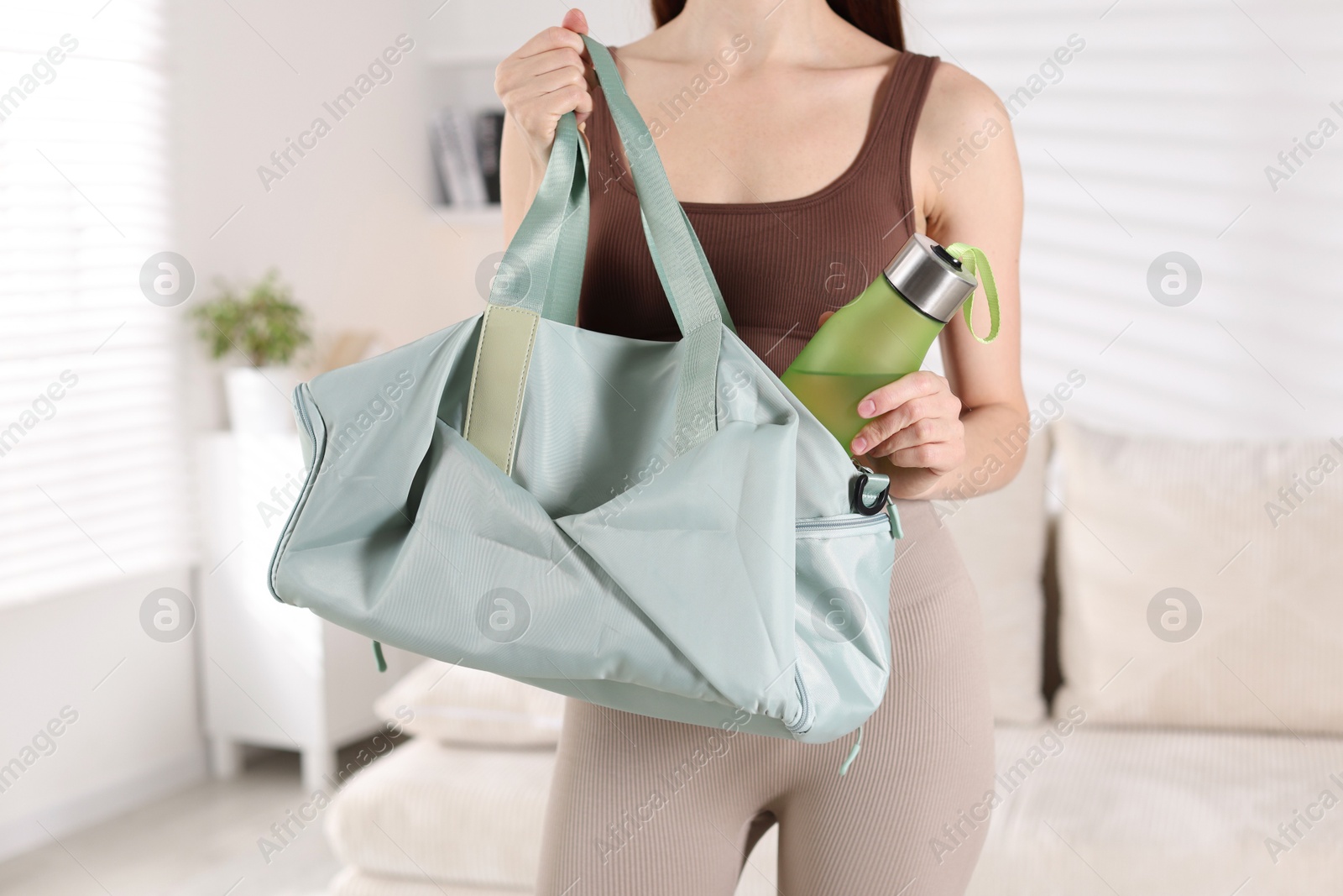 Photo of Woman with gym bag and water bottle at home, closeup