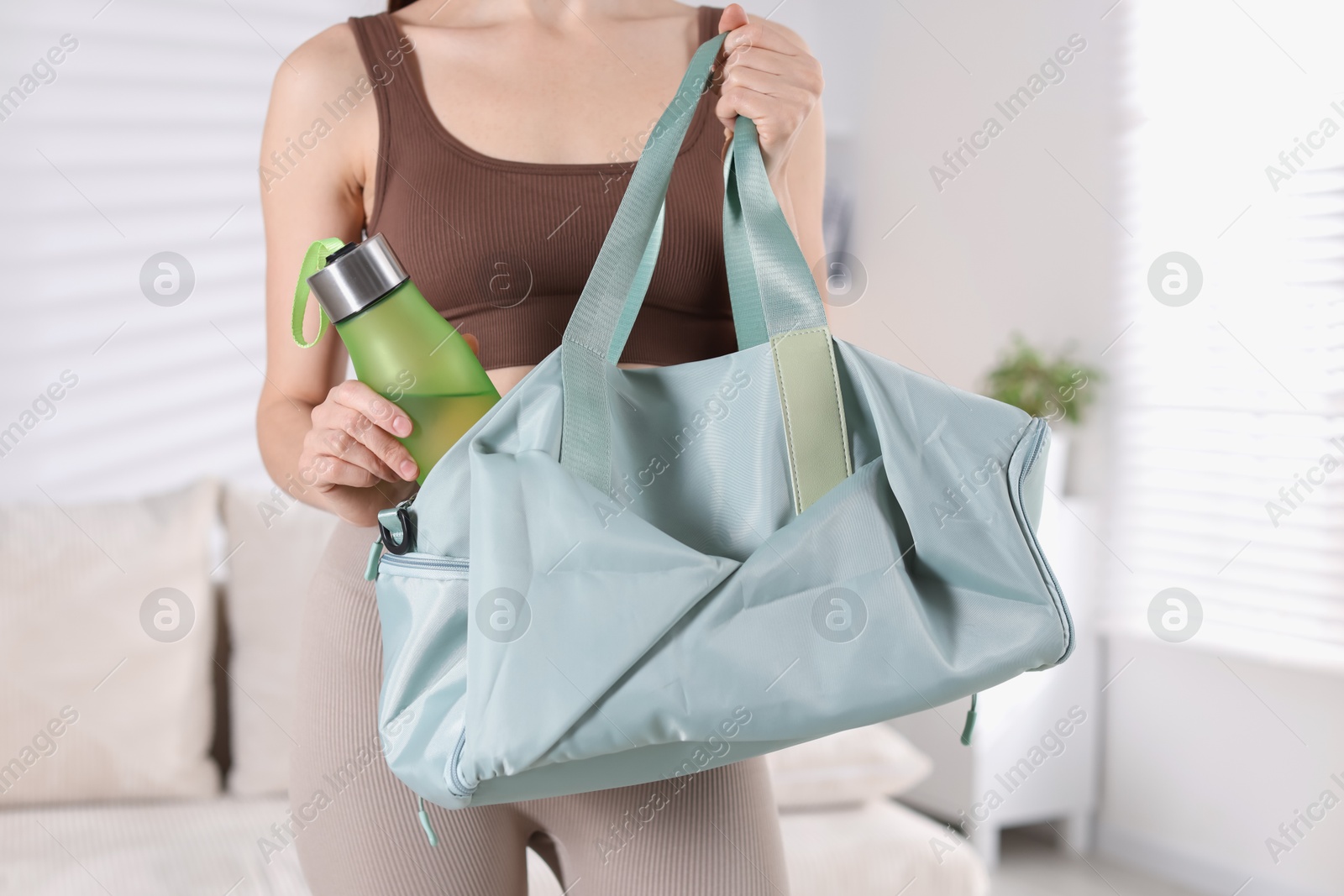 Photo of Woman with gym bag and water bottle at home, closeup