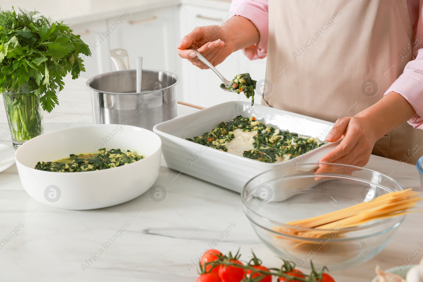 Photo of Woman making spinach lasagna at marble table indoors, closeup