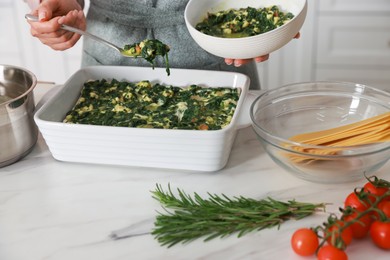 Photo of Woman making spinach lasagna at marble table indoors, closeup