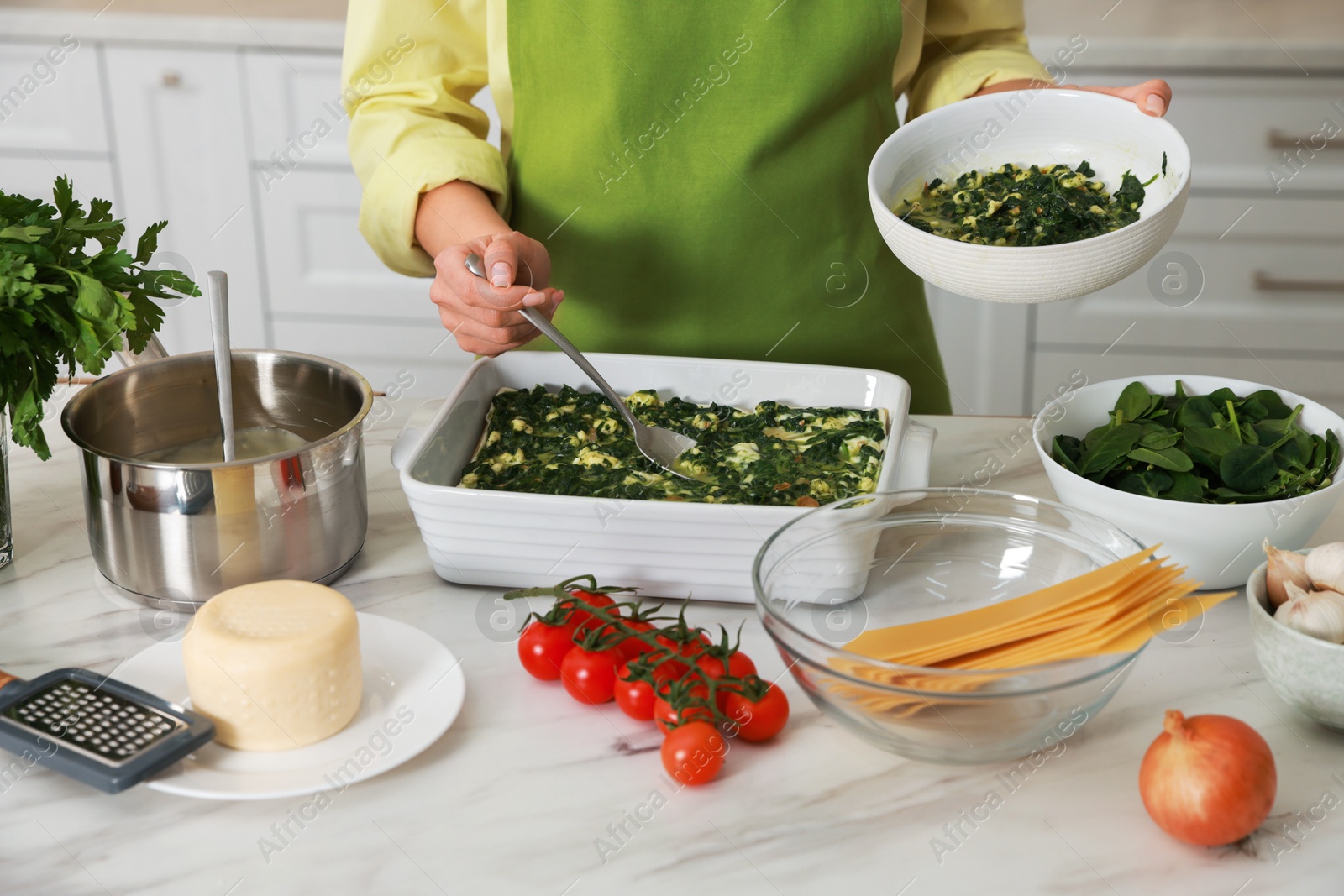 Photo of Woman making spinach lasagna at marble table indoors, closeup