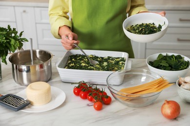 Photo of Woman making spinach lasagna at marble table indoors, closeup