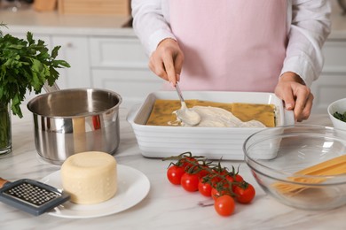 Woman spreading bechamel sauce onto spinach lasagna at marble table indoors, closeup