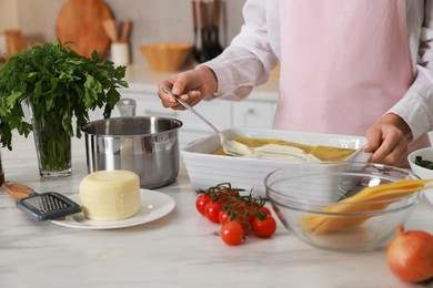 Photo of Woman spreading bechamel sauce onto spinach lasagna at marble table indoors, closeup