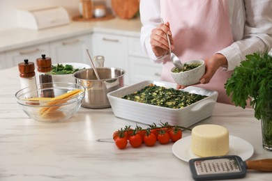 Photo of Woman making spinach lasagna at marble table in kitchen, closeup