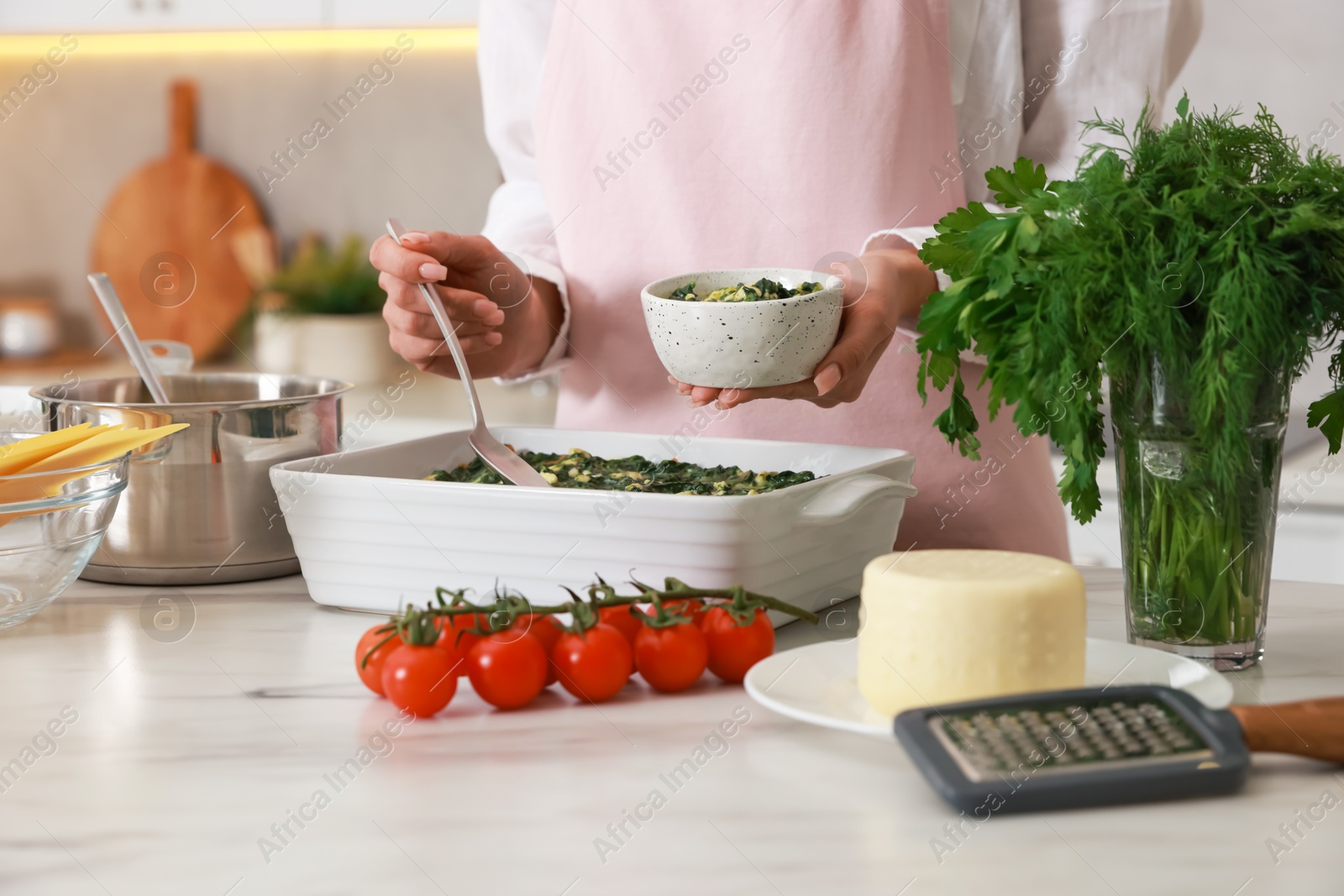 Photo of Woman making spinach lasagna at marble table indoors, closeup