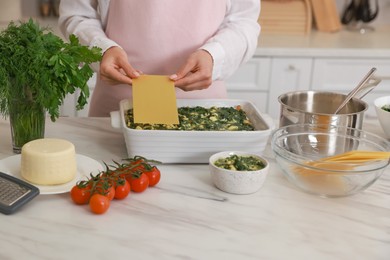 Photo of Woman making spinach lasagna at marble table indoors, closeup