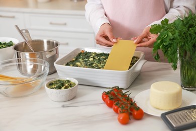 Woman making spinach lasagna at marble table indoors, closeup