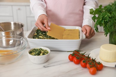 Woman making spinach lasagna at marble table indoors, closeup