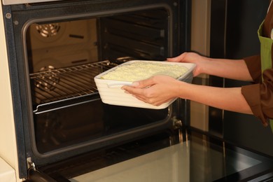 Woman putting baking dish with spinach lasagna into oven, closeup