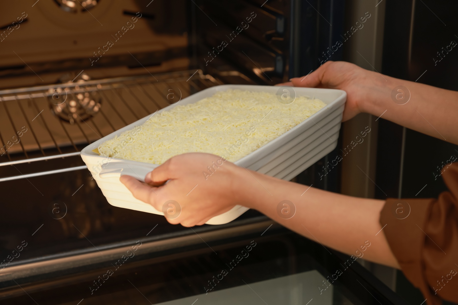 Photo of Woman putting baking dish with spinach lasagna into oven, closeup