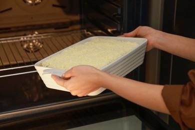 Woman putting baking dish with spinach lasagna into oven, closeup