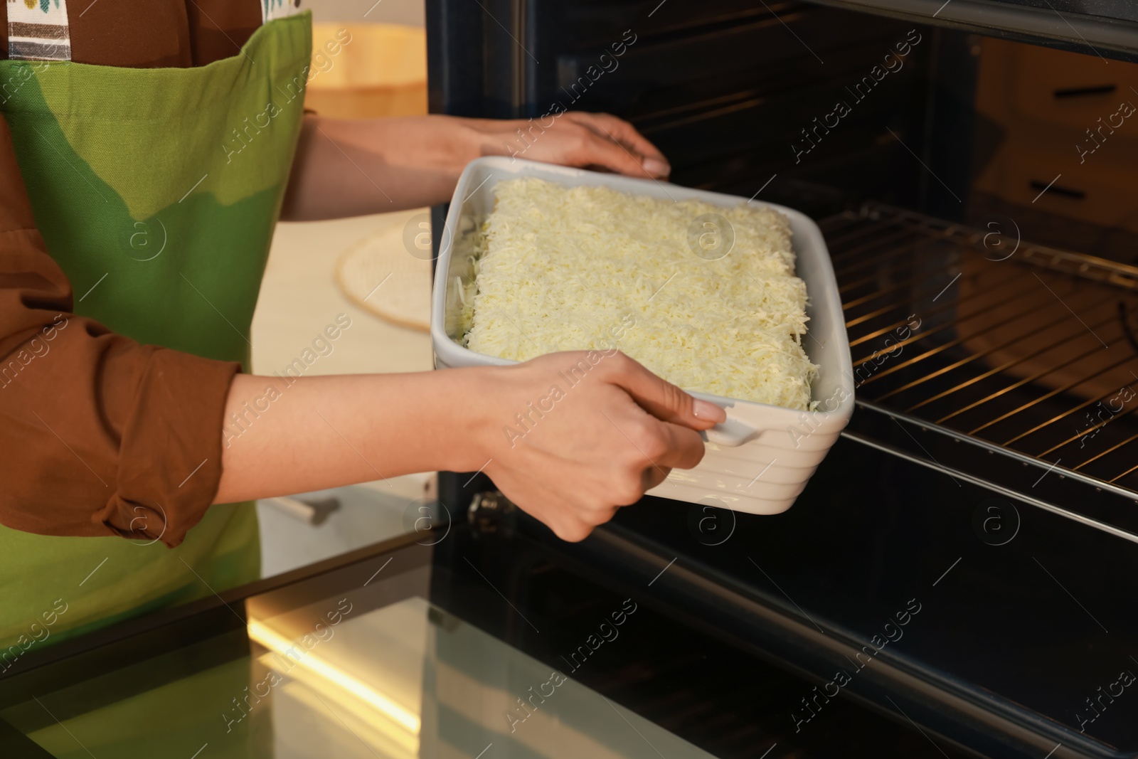 Photo of Woman putting baking dish with spinach lasagna into oven indoors, closeup