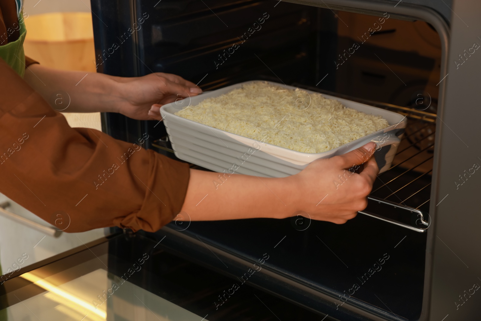 Photo of Woman putting baking dish with spinach lasagna into oven indoors, closeup