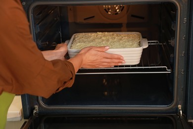 Woman putting baking dish with spinach lasagna into oven, closeup