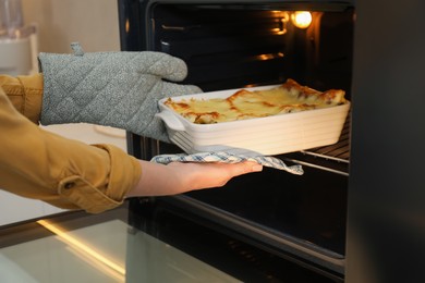 Photo of Woman taking baking dish with tasty lasagna out of oven, closeup