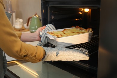 Photo of Woman taking baking dish with tasty lasagna out of oven in kitchen, closeup