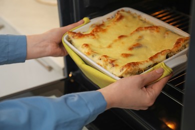 Photo of Woman taking baking dish with tasty lasagna out of oven in kitchen, closeup