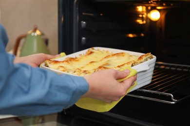 Photo of Woman taking baking dish with tasty lasagna out of oven in kitchen, closeup