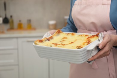 Photo of Woman holding baking dish with tasty lasagna in kitchen, closeup. Space for text