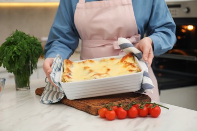 Photo of Woman putting baking dish with tasty lasagna onto white marble table indoors, closeup