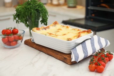 Photo of Tasty lasagna, tomatoes and herbs on white marble table indoors