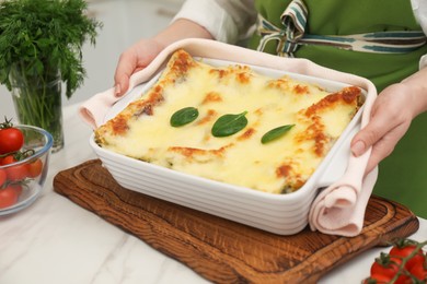 Photo of Woman putting baking dish with tasty spinach lasagna onto white marble table indoors, closeup