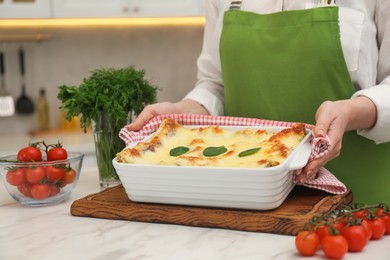 Photo of Woman putting baking dish with tasty spinach lasagna onto white marble table indoors, closeup