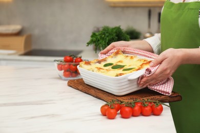 Photo of Woman putting baking dish with tasty spinach lasagna onto white marble table indoors, closeup. Space for text