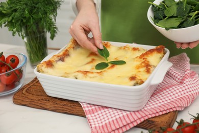 Photo of Woman putting spinach onto lasagna at white table indoors, closeup